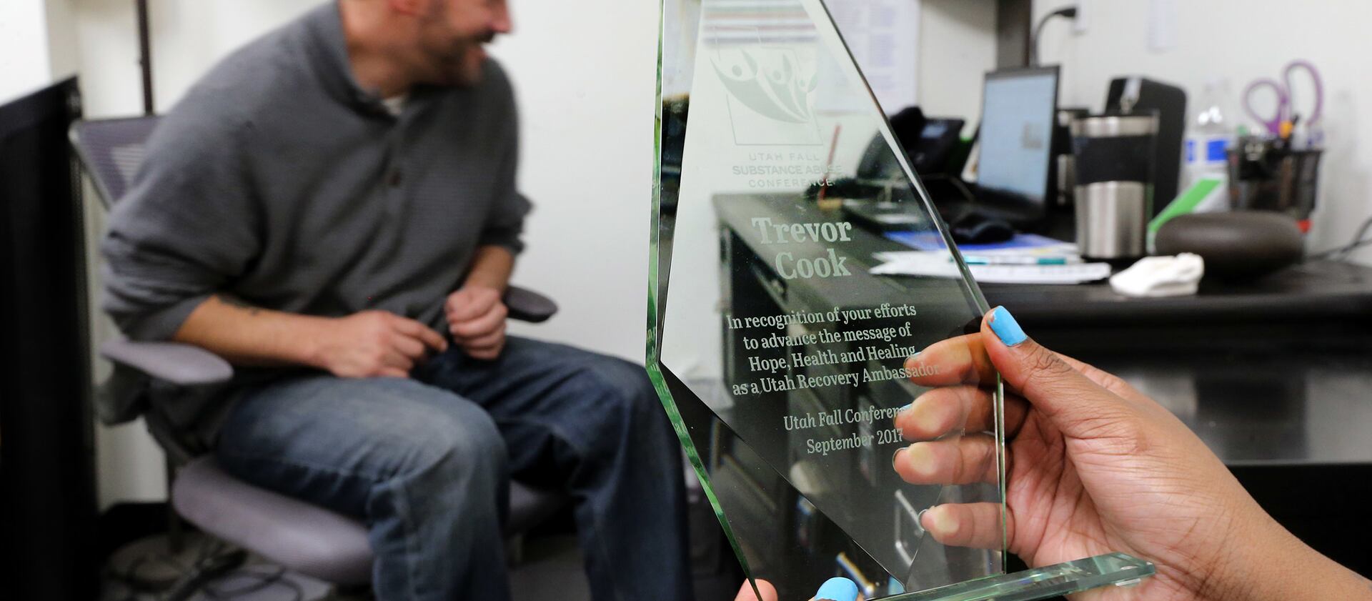 Shantel Cozart holds an award that Trevor Cook, a recovering addict, received as she talks with him at his USARA in his Salt Lake City office on Friday, Dec. 8, 2017.