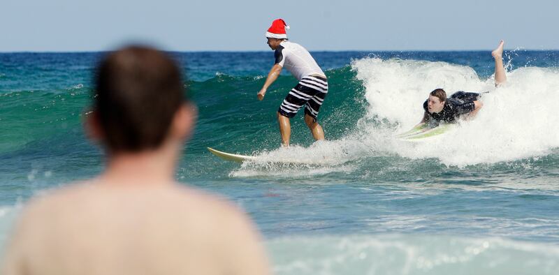 A man wearing a Santa hat surfs on Sydney’s Bondi Beach as thousands flock to the ocean to celebrate Christmas.
