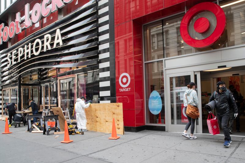 A shopper leaves the Target Store on 34th St. with supplies as carpenter board up the Sephora story, Friday, March 20, 2020, in New York.