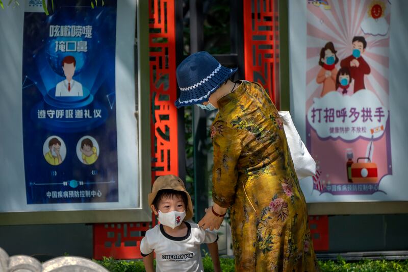 A woman and boy wearing face masks walk near posters encouraging people to wear masks and avoid handshakes in Beijing.