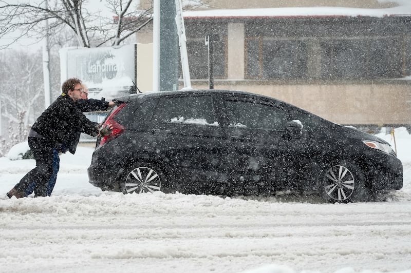 People push a car out of a snowbank as a winter storm arrives in West Allis, Wis.