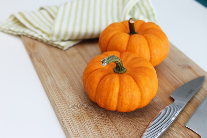 Two pumpkins sit on a cutting board.