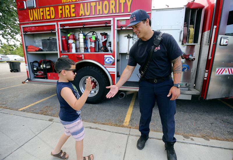 Bentley Miramontes, who wants to be a firefighter, high-fives Unified firefighter Keloni Kamalani during a Night Out Against Crime at Pleasant Green Park in Magna on Monday, Aug. 5, 2019.