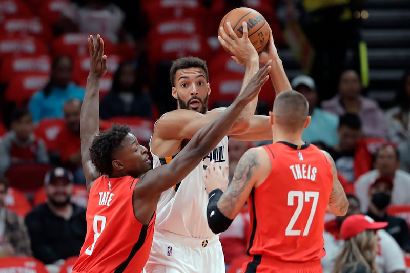 Utah Jazz center Rudy Gobert ooks to pass the ball as Houston Rockets forward Jae’Sean Tate and center Daniel Theis defend.