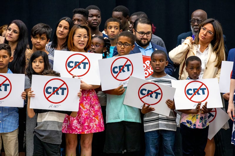 Kids hold signs against critical race theory near Gov. Ron DeSantis as he addresses the crowd before publicly signing HB7.