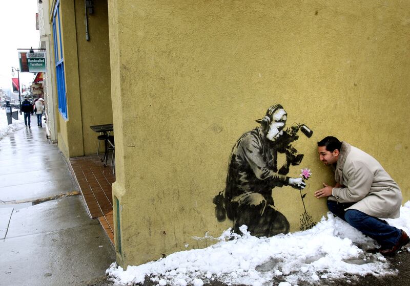 Paul Nanda goofs around while having his photo taken by a friend in front of graffiti that is supposedly the work of Banksy on Main Street in Park City.