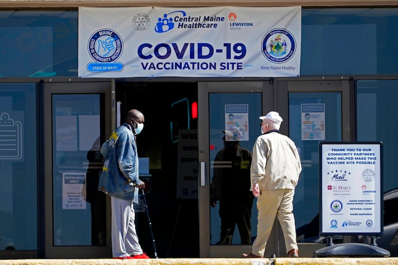 One man holds the door for another as they arrive at a COVID-19 vaccination clinic at the Auburn Mall in Auburn, Maine.