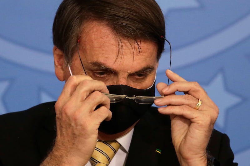 Brazil’s President Jair Bolsonaro removes his glasses over his mask, which he wears due to the COVID-19 pandemic, at an event promoting a government campaign against domestic violence at Planalto presidential palace in Brasilia, Brazil, Friday, May 15, 2020. (AP Photo/Eraldo Peres)