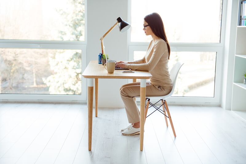 Woman sits at a desk while typing on a laptop.
