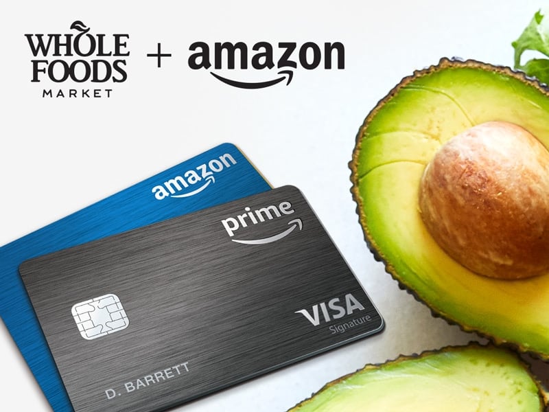 Amazon credit cards sit next to avocados and the Amazon and Whole Foods Market logos.