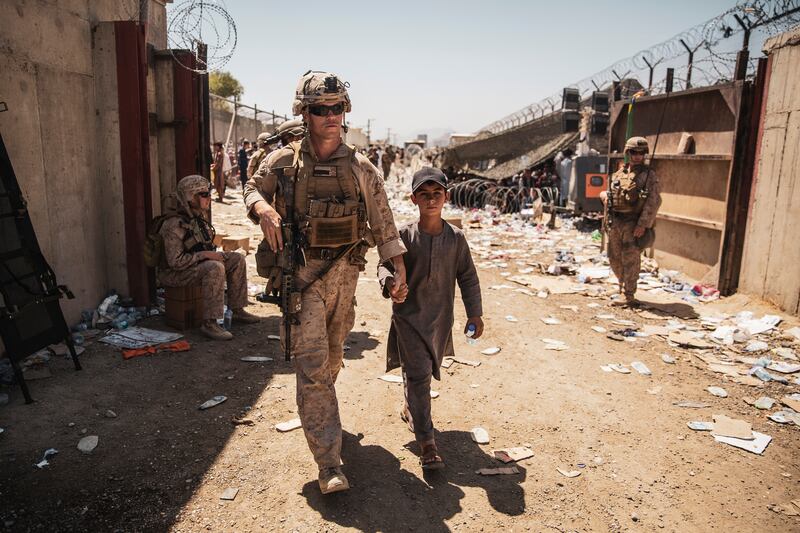 In this image provided by the U.S. Marine Corps, a U.S. Marine escorts a child during ongoing evacuations at Hamid Karzai Airport, Afghanistan.