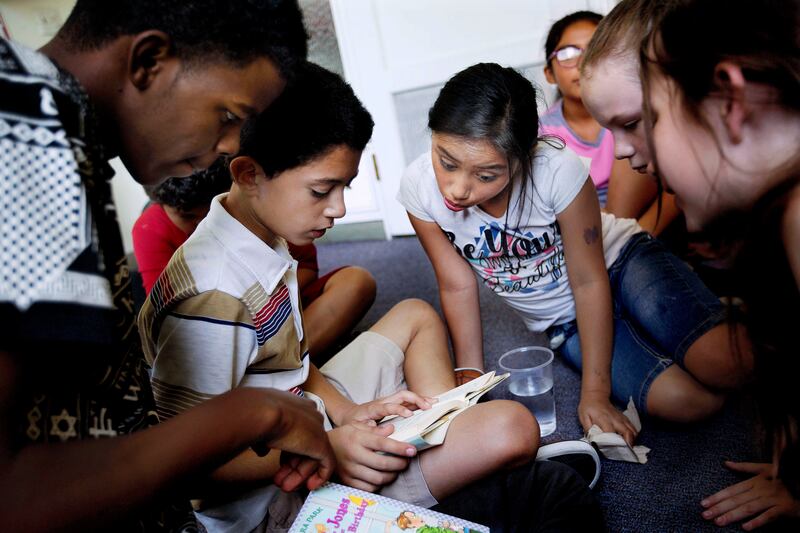 Ahmed Kayliye, left, and a group of girls help Fahed Hamad with his reading at Promise South Salt Lake’s summer camp at the Historic Scott School in South Salt Lake on July 6, 2017.