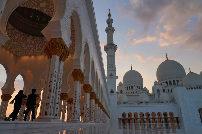 Tourists walk through Sheikh Zayed Grand Mosque at dusk in Abu Dhabi, United Arab Emirates.
