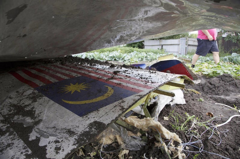 FILE - In this July 23, 2014 file photo, a man walks past a piece of the crashed Malaysia Airlines Flight 17 in a garden in the village of Petropavlivka, Donetsk region, eastern Ukraine. The remains of at least 15 Malaysians killed when the jetliner with