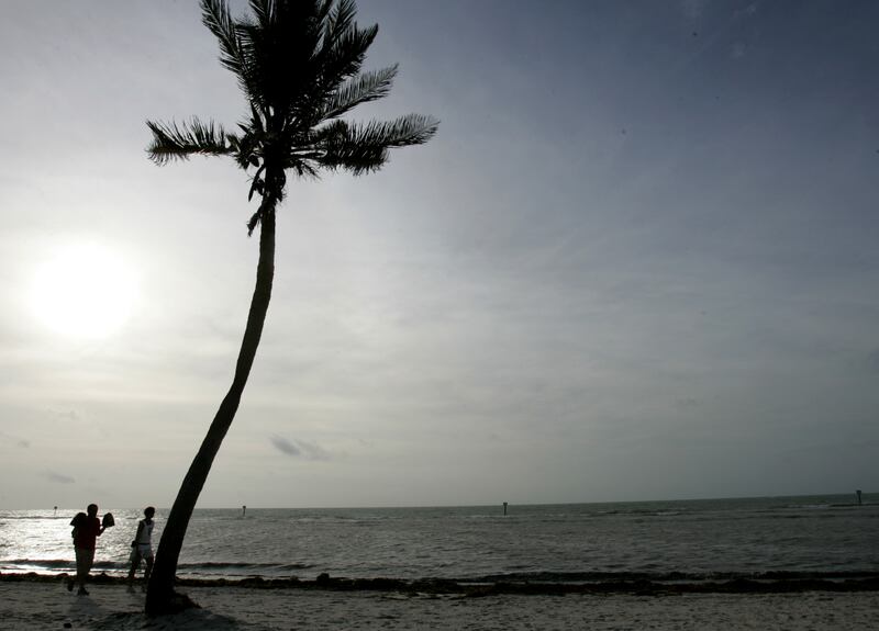 Key West residents walk along the beach on the Atlantic Ocean as the sun shines through the clouds in Key West.