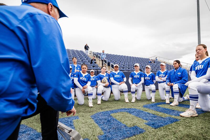Under gray skies, members of the BYU softball team take a knee to listen to their coach prior to game against Oklahoma State on March 23 in Provo. Gray skies and inclement weather are part of recipe of spring sports in Utah.