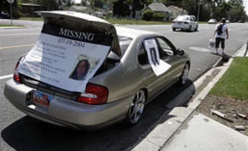 Angie Cardall walks in Provo, followed by her husband in a car festooned with material about Lori Hacking.