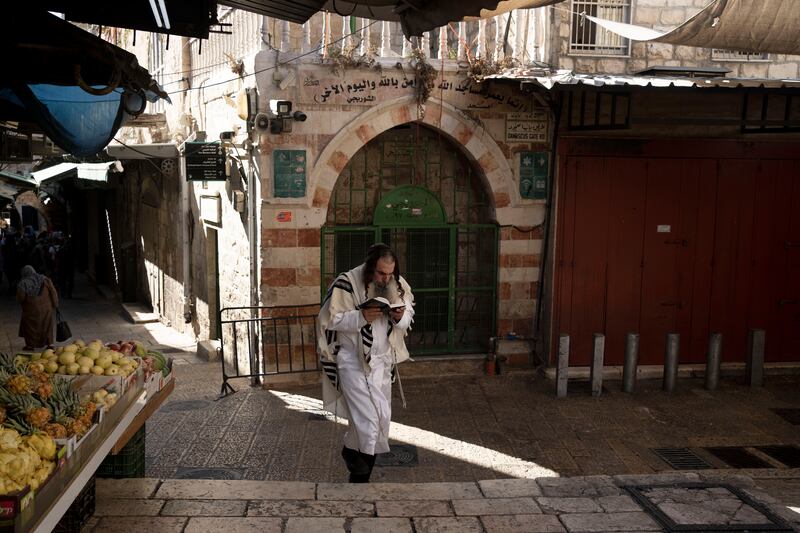 A Jewish worshipper reads from a prayer book on Yom Kippur as he walks in the Old City of Jerusalem, Monday, Sept. 25, 2023.