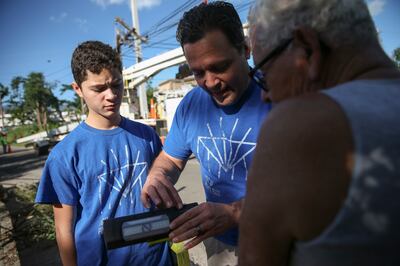 Jorge M. Alvarado, center, and his son, Jorge Daniel Alvarado, explain how to use a solar powered light before giving it to a man they encountered directing traffic around a work crew installing new power poles in Juana Díaz, Puerto Rico, on Saturday, Dec