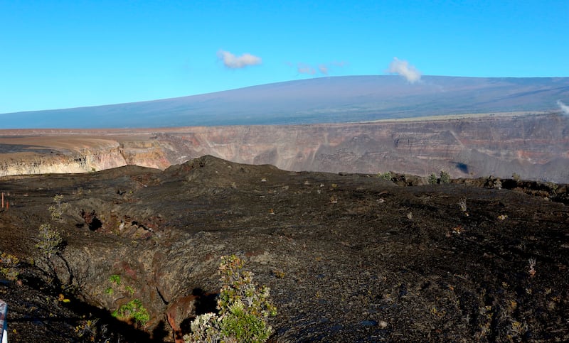 Hawaii’s Mauna Loa volcano towers over the summit crater of Kilauea volcano in Hawaii Volcanoes National Park on the Big Island.