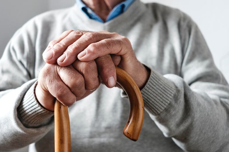 The folded hands of an elderly man resting on a walking cane.