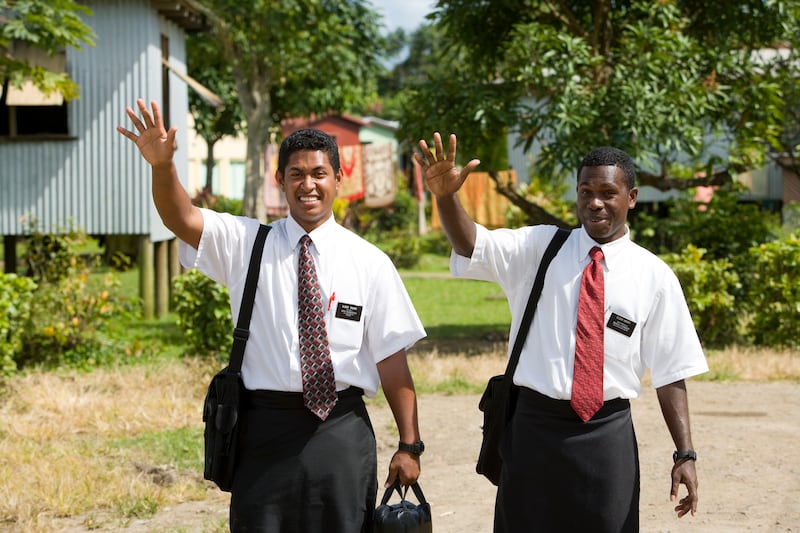 Two missionaries of The Church of Jesus Christ of Latter-day Saints serving in Fiji wave a friendly hello.