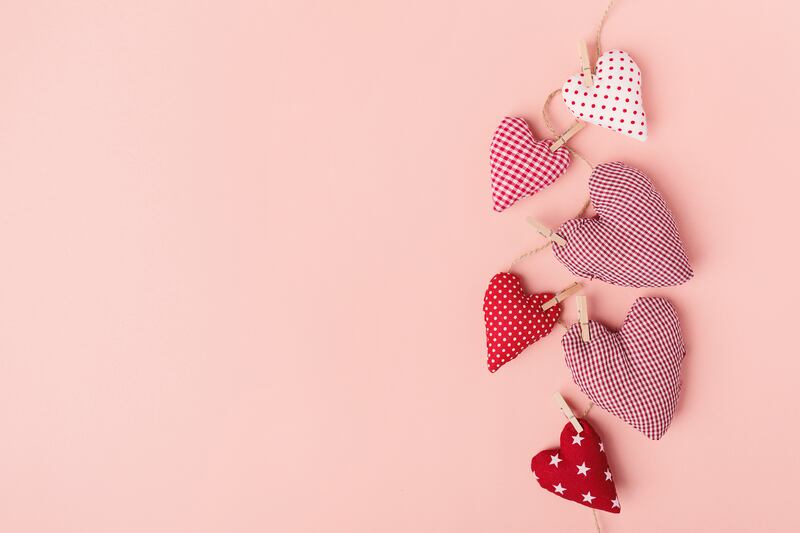 Fabric hearts clipped to a string with clothes pins cross both sides of the string against a pink background.