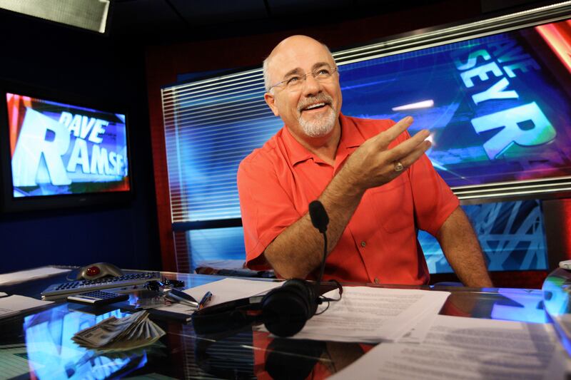 Dave Ramsey, a conservative media figure and financial expert, smiles sitting at a desk in his broadcasting studio.