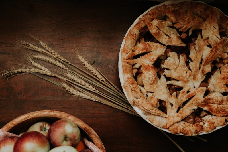 An apple pie sits on a table near a bushel of apples.