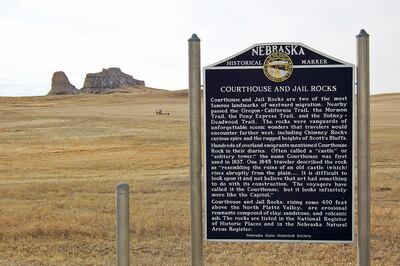 Historical panel interpreting Courthouse Rock and Jail Rock, seen in the distance in Morrill County, Nebraska. Jail Rock is seen at the left with Courthouse Rock at the right.