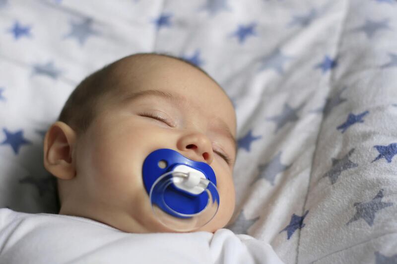 Close up of sleaping baby with blue soother on white blankt with blue stars