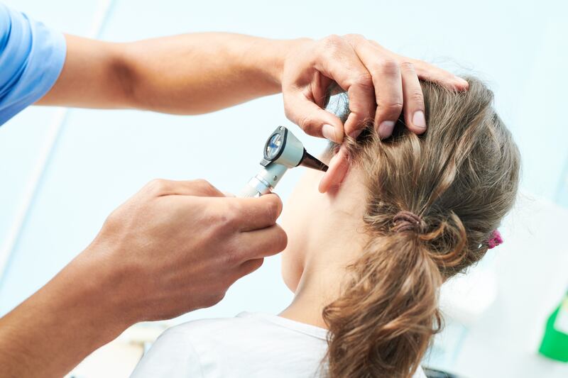 A pediatrician examines a girl’s ear with an otoscope.
