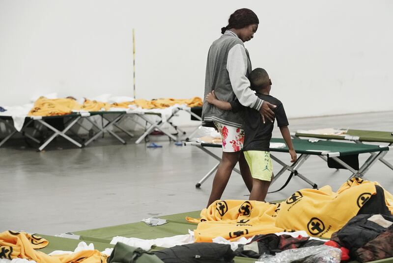 Valeria Lamour walks with son Abisay Lamour through a center full of cots with orange blankets.