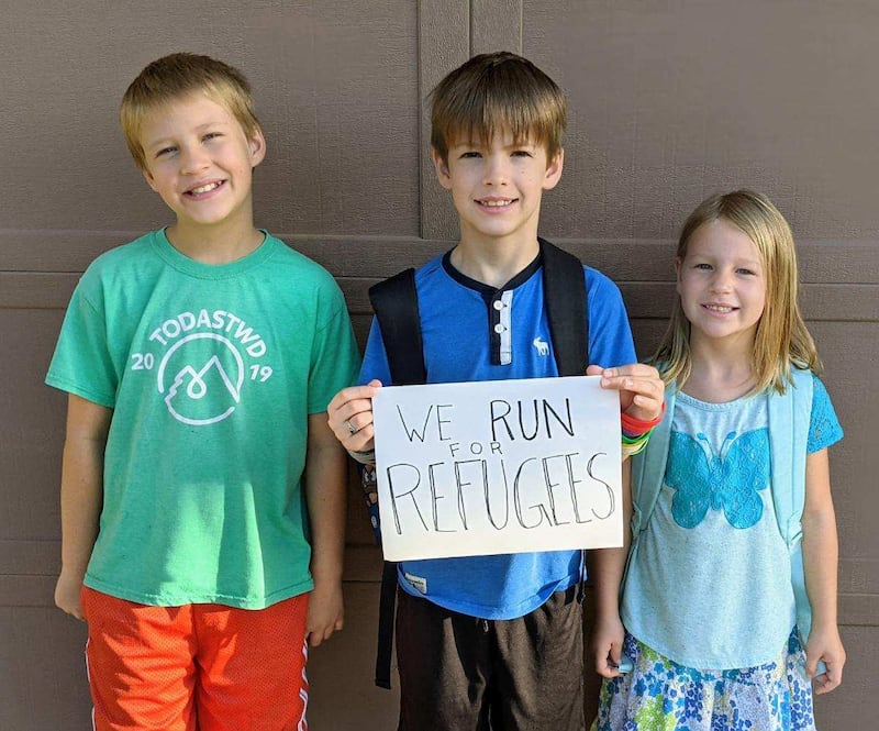 A 10-year-old boy holds a sign that says “We run for refugees.”