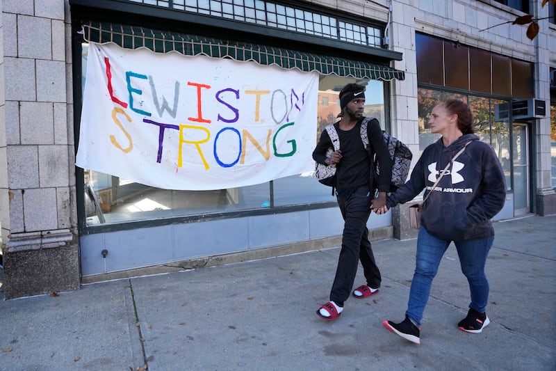 A couple walks by a banner that was put up in response to this week’s deadly mass shootings, on Oct. 27, 2023, in Lewiston, Maine.