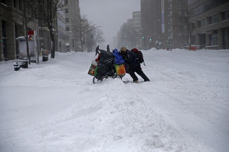 A homeless man pushes a cart with his belongings across 13th Street in downtown Washington, Saturday, Jan. 23, 2016. Millions of people awoke Saturday to heavy snow outside their doorsteps, strong winds that threatened to increase through the weekend, and