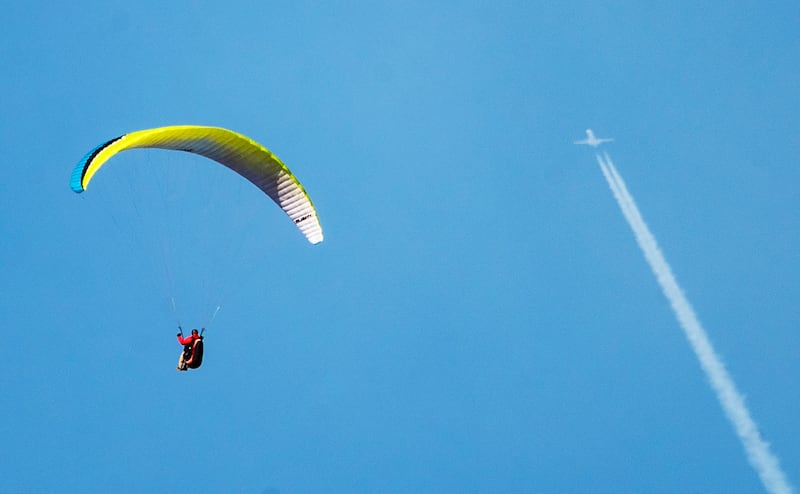 A paraglider flies high near Francis Peak as an airliner passes overhead.